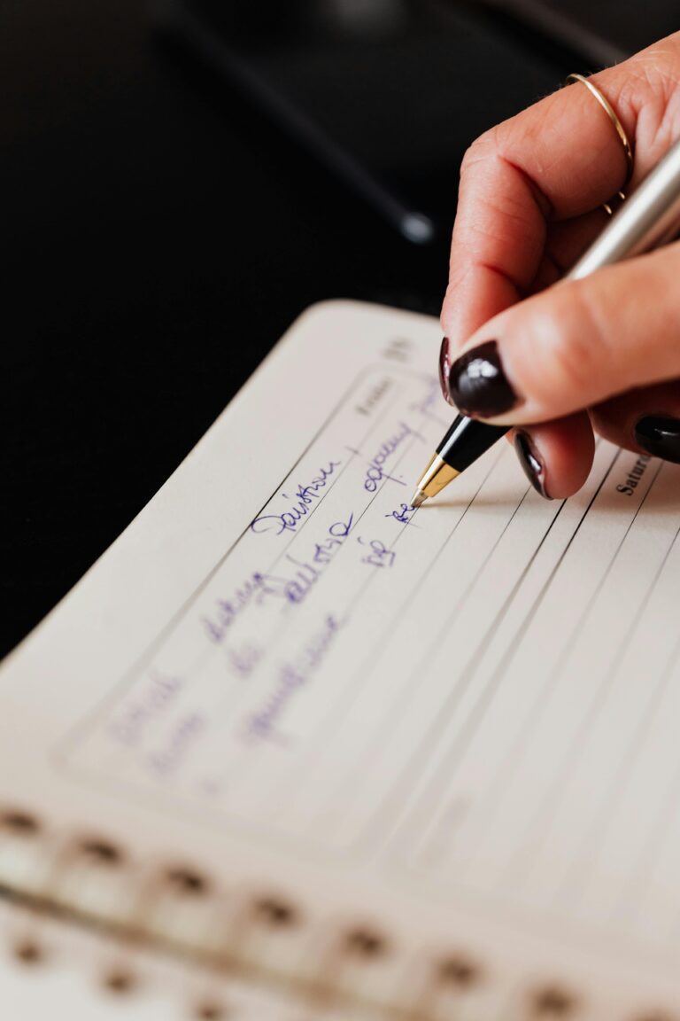 Crop anonymous female with planner and pen writing down important information while sitting at black desk